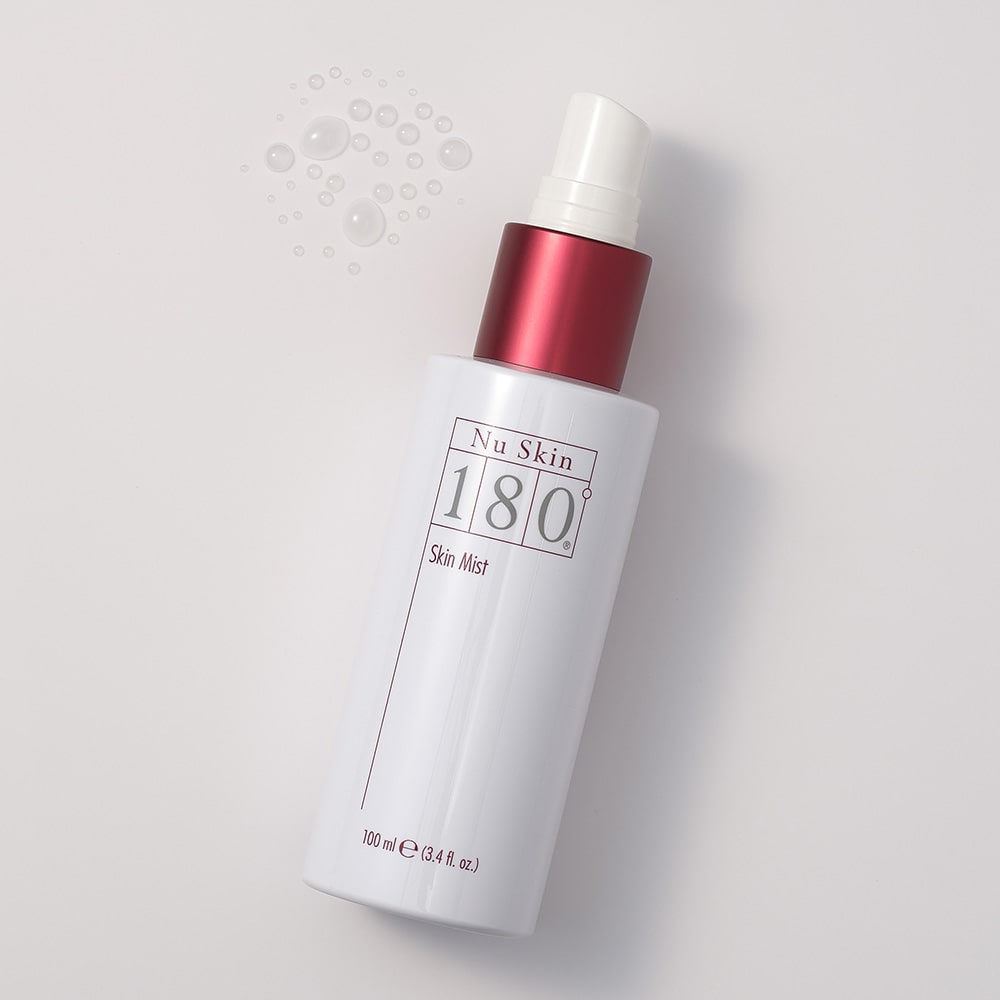 Nu Skin 180° Skin Mist (100ml) liegt ohne Verschlusskappe auf glatter Oberfläche. Daneben wurden vereinzelte Tropfen des transparenten Gesichtswassers aufgetragen.