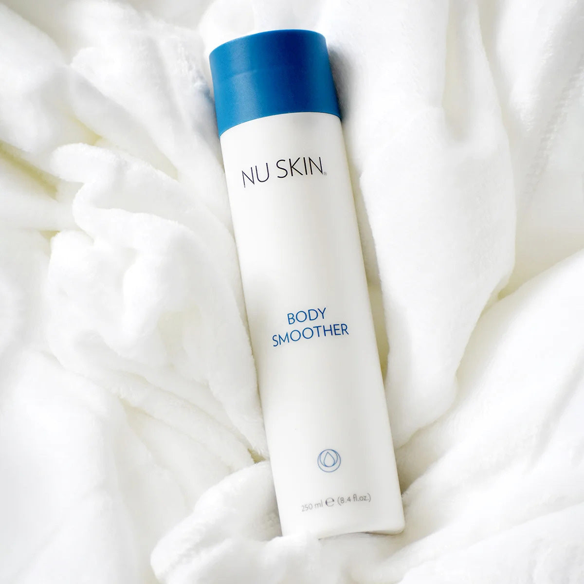 NuSkin Body Smoother Flasche (250ml) liegt geschlossen inmitten flauschigem weißen Handtuch.