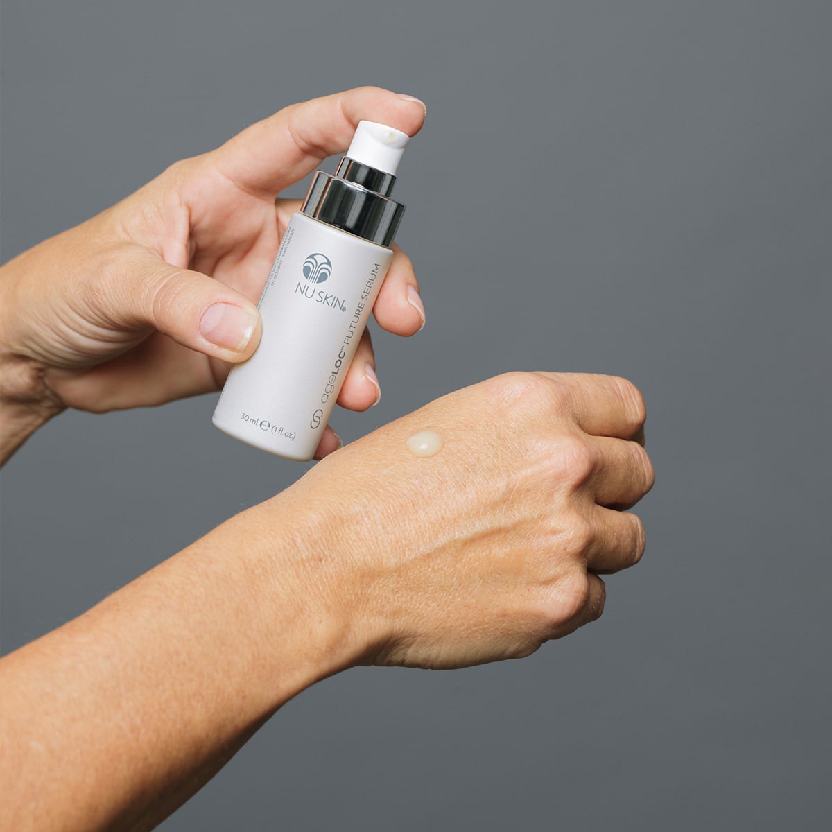 ageLOC® Future Serum wird vor grauem Hintergrund auf den Handrücken einer Frau aufgetragen. Das Serum ist leicht durchscheinend und eher liquide.