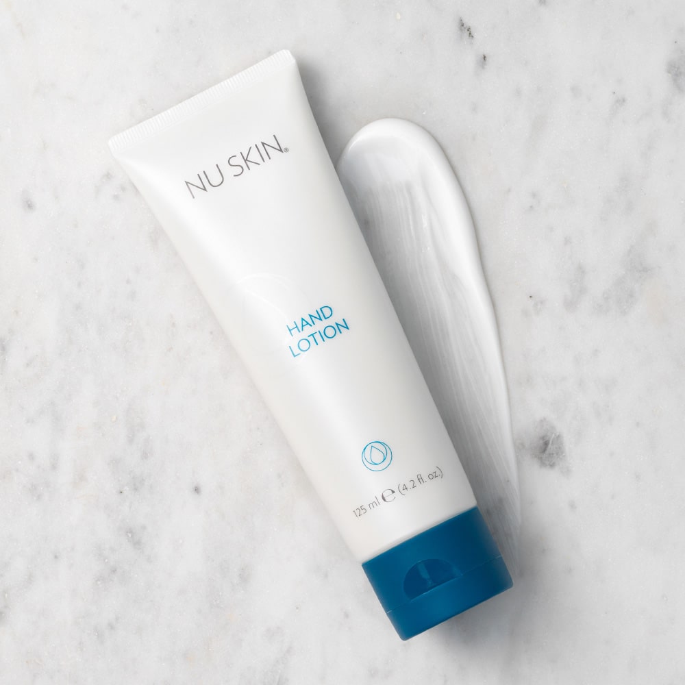 Hand Lotion von NuSkin (125ml) liegt auf marmorner Oberfläche. Hinter die Tube wurde eine großzügige Konsistenzprobe der weißen liquiden Lotion gegeben.