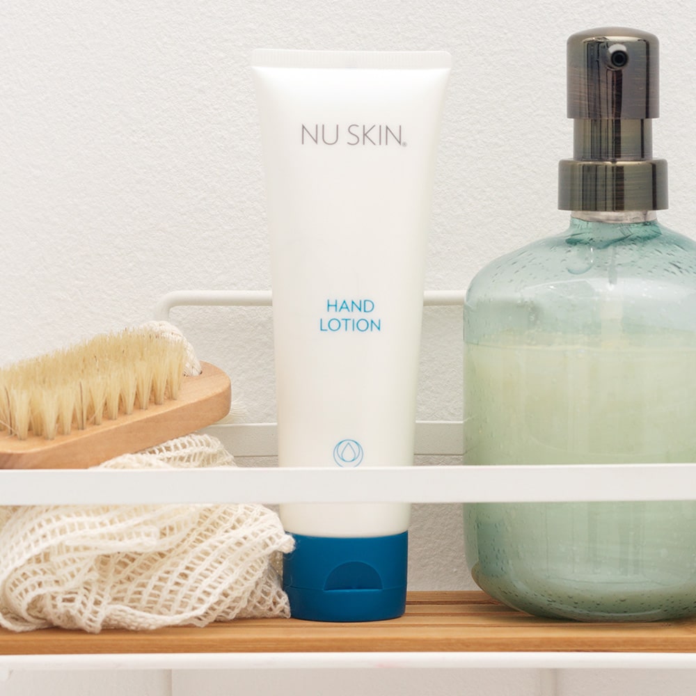 NuSkin Hand Lotion Tube (125ml) steht in sanitärer Umgebung zwischen Schwamm und Seifenspender.